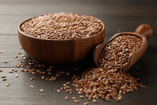 Flax seeds in bowl and scoop on wooden table, closeup