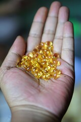 Fototapeta premium Close-up of a human hand holding a pile of golden yellow softgel fish oil capsules.