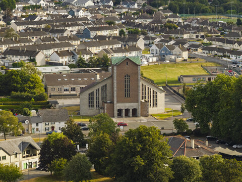 Aerial view of the Church of the Resurrection with its distinctive green copper roof and brick facade, surrounded by residential rooftops and lush trees in Mallow, County Cork, Ireland.