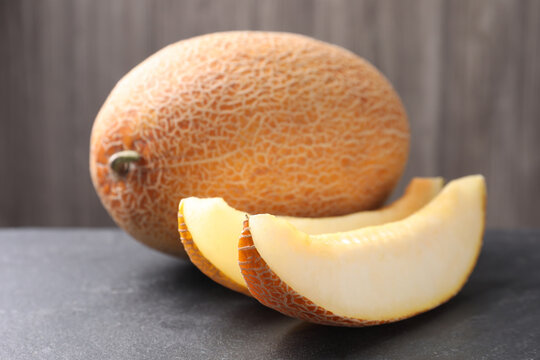Whole and cut ripe melons on black table, closeup