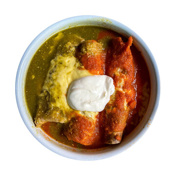 A bowl of traditional Mexican enchiladas split down the middle with vibrant green salsa verde and red salsa, melted cheese, and a dollop of sour cream on top.