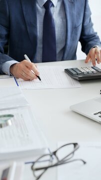 Close up of calculator while male accountant calculating taxes and analyzing financial data in office setting. Audit and taxes in business