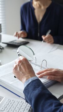 Two professional chartered accountants reviewing financial reports and analyzing data using a calculator and a magnifying glass, ensuring accuracy and compliance. Audit and taxes in business