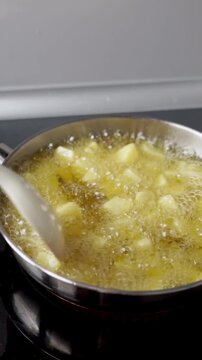 Diced potatoes for patatas bravas frying with olive oil in a frying pan on a ceramic stove
