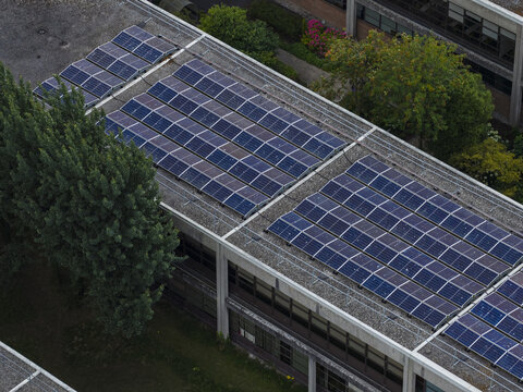 Aerial view of the solar panel array installed on the flat roof of the University of Galway Research and Innovation Centre, surrounded by green trees in Galway, County Galway, Ireland.