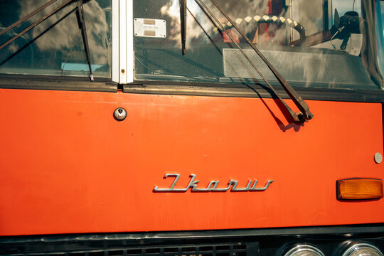 08.13.2026 - Minsk, Belarus: A close-up view of the front of a vintage orange Ikarus bus showing its windshield, wipers, and chrome emblem.