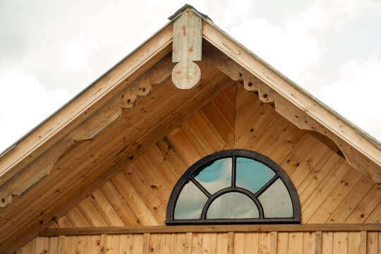 A wooden roof gable features decorative carved trim and a semi-circular arched window reflecting the sky.