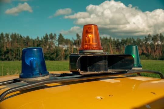 Emergency vehicle lights featuring blue, orange, and green beacons mounted on a roof against a sky and forest background.