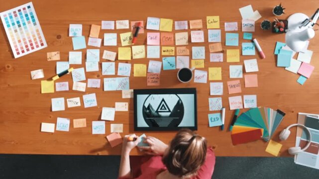 Top view of business team write graphic logo on meeting table with colorful sticky notes and design while explain idea. Project manager sharing idea and explain concept art to smart team. Symposium.