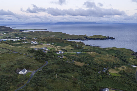 Aerial view of the coastal landscape of Doonin with scattered houses, green rolling hills, a winding road, and the Atlantic Ocean in Doonin, County Donegal, Ireland.