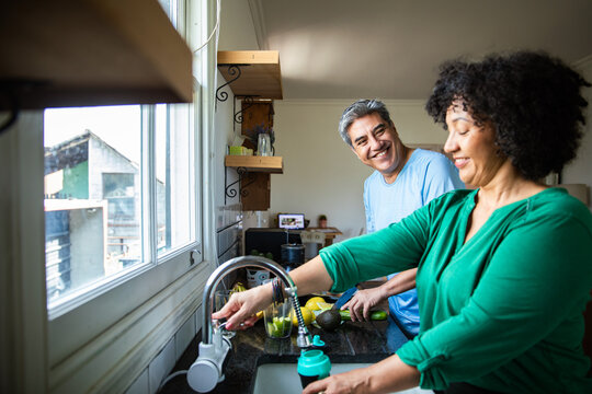 Smiling mature couple preparing healthy smoothie in home kitchen