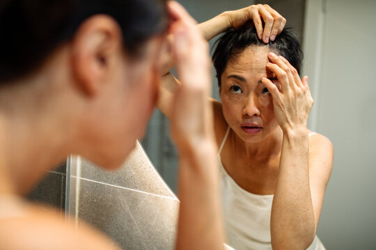 Middle-aged woman checking hairline in home bathroom mirror