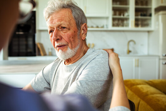 Concerned senior man comforted by caregiver in home kitchen