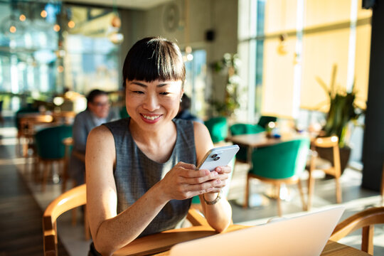 Smiling woman using smartphone at cafe workspace