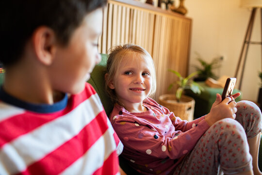 Smiling siblings relaxing with smartphone at home