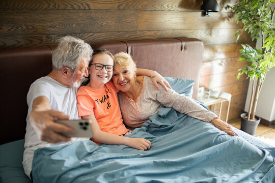 Grandparents taking selfie with granddaughter in bed at home