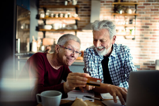 Smiling senior couple paying bills online at home kitchen