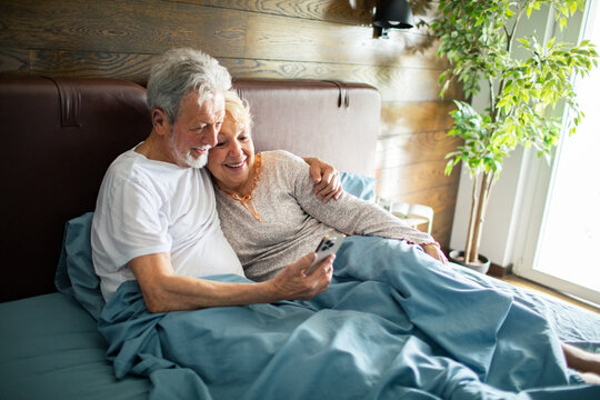 Senior couple in bed using smartphone at home