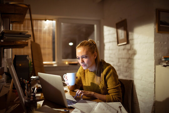 Young woman working late in a home office with laptop and coffee