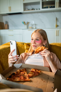 Young woman with eye patches eating pizza and using smartphone at home
