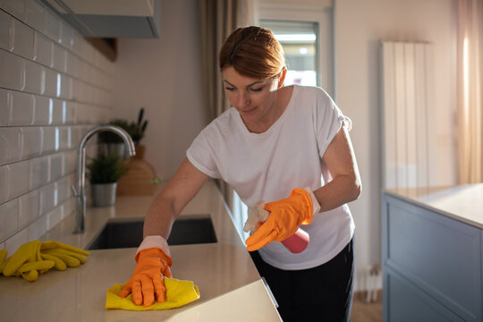 Woman cleaning kitchen countertop with spray at home