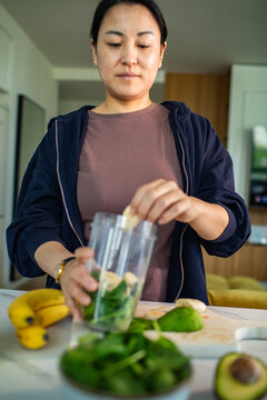Woman preparing green smoothie in home kitchen