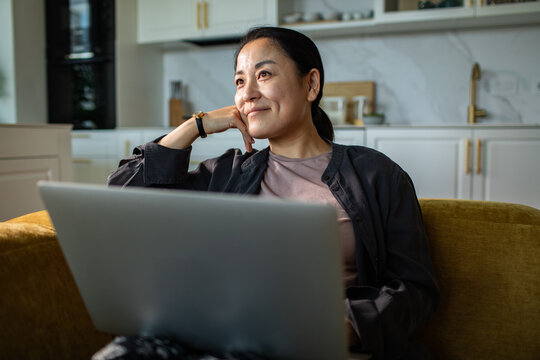 Smiling woman working on laptop in home kitchen
