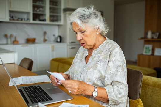 Senior woman shocked by bills on laptop at home