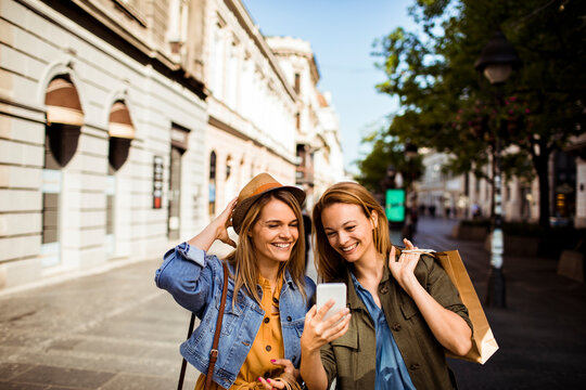 Two female friends shopping and using smartphone on city street