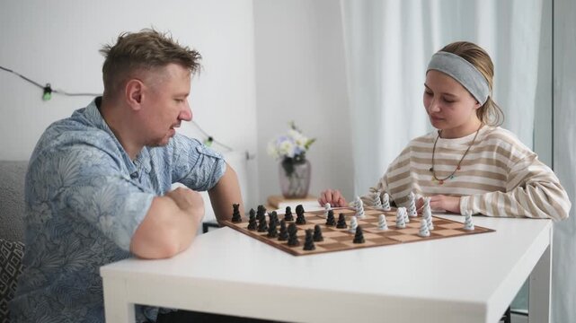 Father and daughter play chess indoors.
