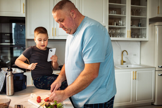 Father and son making lunch together in modern home kitchen