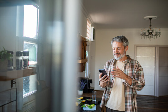 Smiling middle-aged man using smartphone in home kitchen