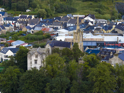 Aerial view of Donegal Castle and St. Patrick's Church surrounded by historic town buildings, lush green trees, and rooftops in Donegal, County Donegal, Ireland.