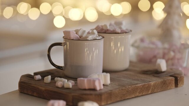 Two Mugs Of Hot Cocoa In A Christmas-Decorated Kitchen With Blurred Garland Lights