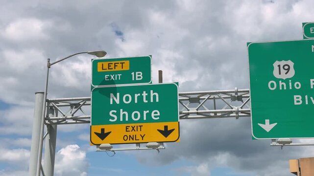 Highway sign directs motorists toward Pittsburgh's North Shore at Exit 1B beneath a cloudy sky, representing urban travel and transportation. 15322  