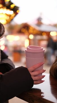 Girl Holds Cups Of Hot Mulled Wine At A Christmas Market Against Garland Lights, Vertical Video