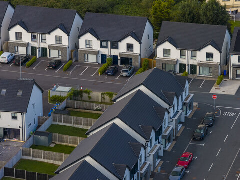 Aerial view of modern residential houses with dark roofs and white walls, featuring paved driveways, parked cars, and small gardens in Donegal, County Donegal, Ireland.