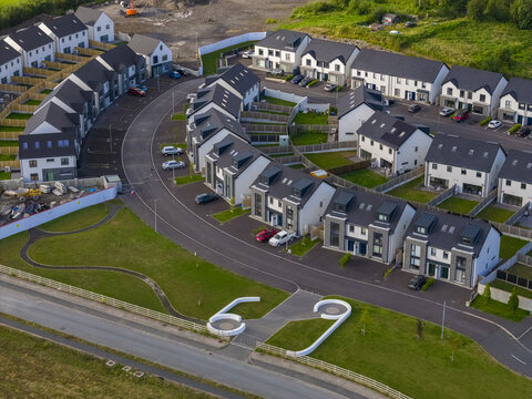 Aerial view of a modern residential housing development with white and grey houses, paved roads, and green lawns in Donegal, County Donegal, Ireland.