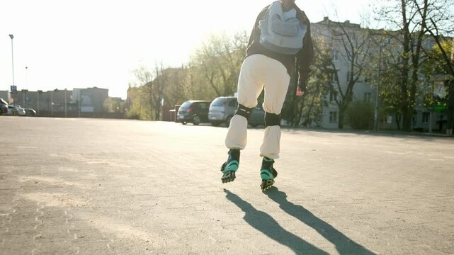 Girl wearing inline skates and a backpack glides on a large paved lot. Sun creates bright backlight and long shadows.