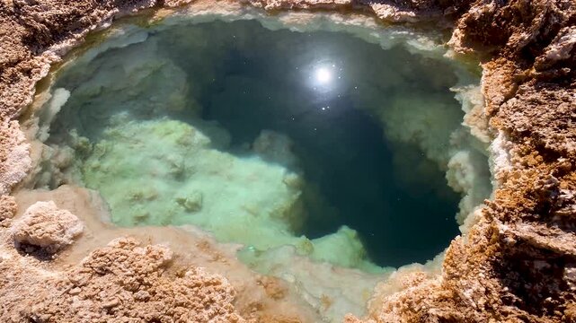 Salty water flowing slowly within ojos del salar lagoon in the atacama desert, a small but deep body of water surrounded by salt crust with the bright sun reflecting on the surface