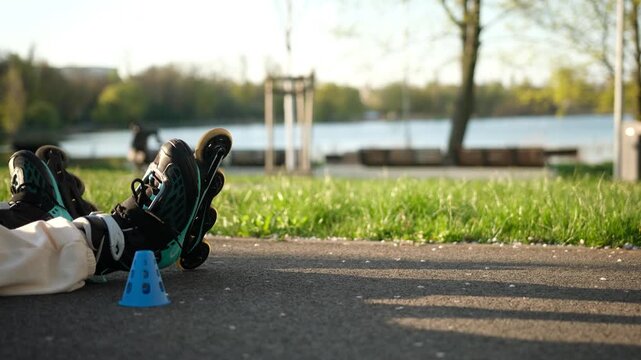 Black and teal inline skates sit on an asphalt path next to a blue cone.