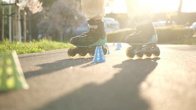Girl on black and teal roller skates navigates colorful cones on a paved path. Warm sunlight creates long shadows.