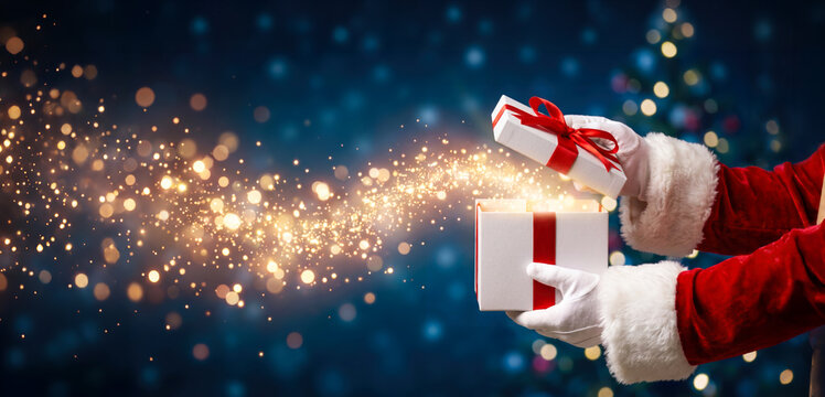 A person wearing a red Santa suit holds one gift box while opening another box. Sparkles float out of the opened box. This scene happens during the holiday season
