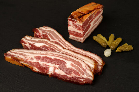 Smoked pork belly slices with pickles on black background