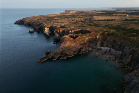 Aerial view over Flimston Bay, Wales, showing rugged sea cliffs, rocky headlands and clear blue-green coastal water.