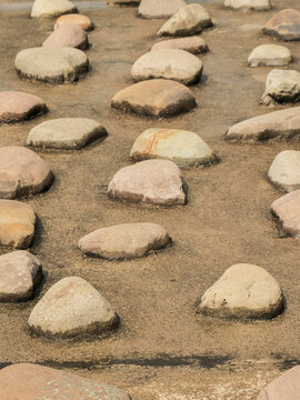 Rough stones line water's edge, sunlit and weathered. Pebbles rest on sandy shore near calm, shallow water. Image ideal for nature, coastal, or travel-themed projects