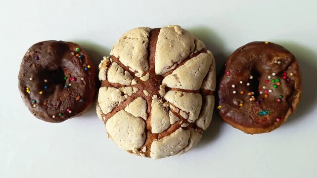 Traditional sweet bread concha flanked by two chocolate glazed doughnuts isolated on white background