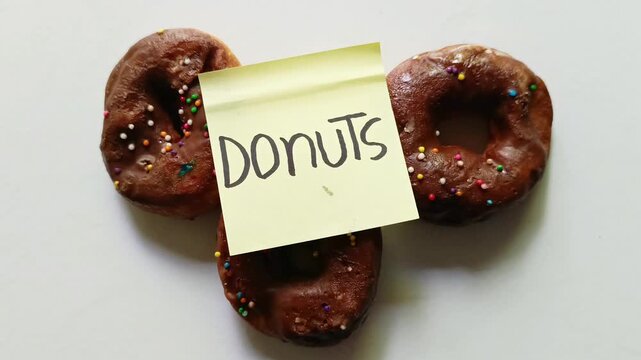 Three chocolate glazed doughnuts with handwritten donuts note isolated on white background