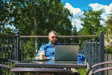 Fototapeta premium Middle aged businessman working remotely with laptop at outdoor cafe terrace. workspace for productive summer office and digital lifestyle.