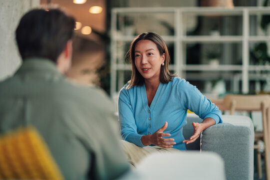 Asian businesswoman communicating with male colleague, discussing project, collaborating in modern office lounge